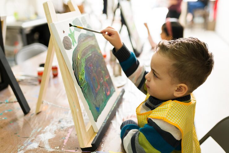 side-view-handsome-elementary-boy-doing-some-final-touches-his-painting-his-art-class_662251-145